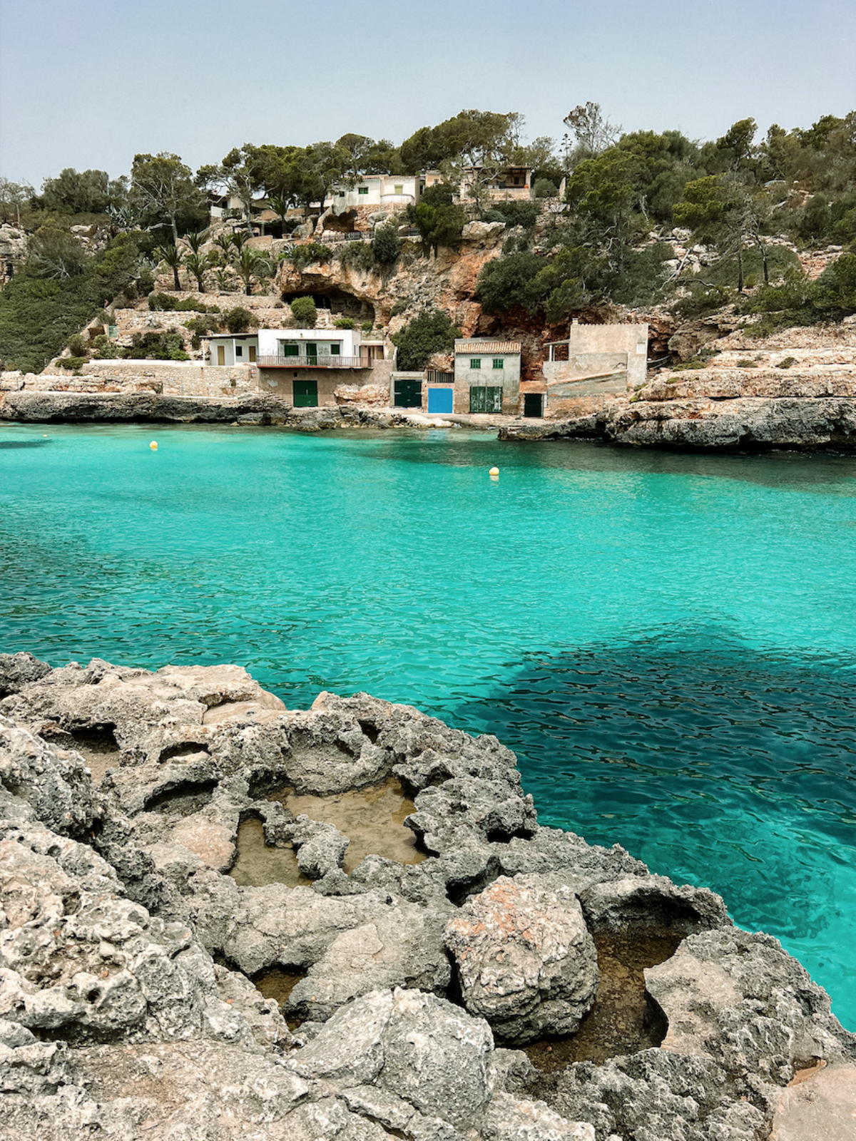 Coastal scene with turquoise water, rocky foreground, and houses on a hillside.