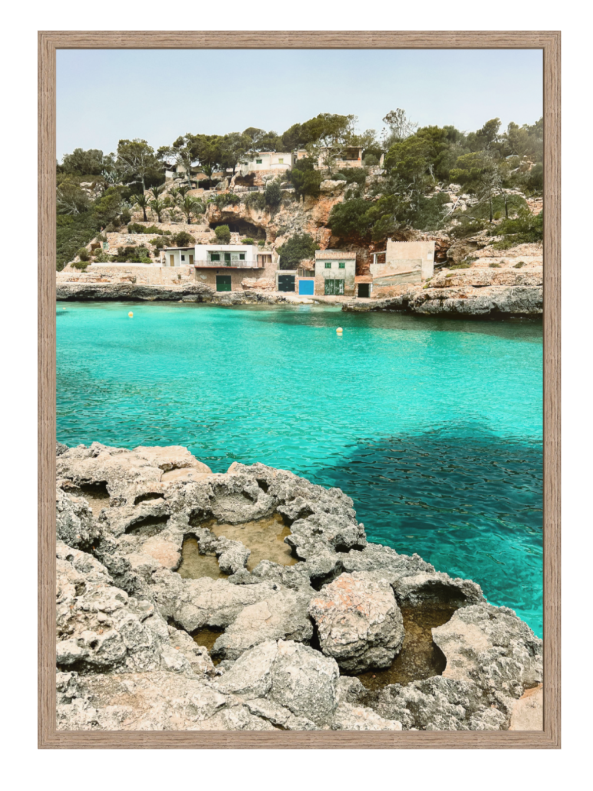 Framed artwork of a coastal scene with turquoise water and rocky shoreline. hazel frame