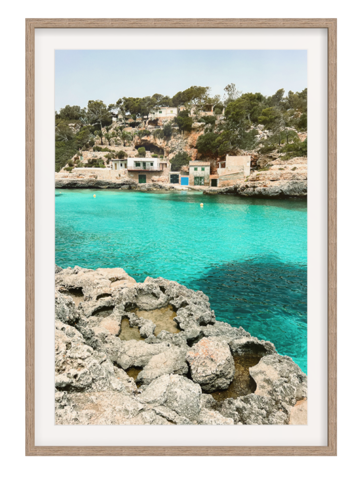 Framed photograph of a coastal scene with clear blue water and rocky hazel foreground.