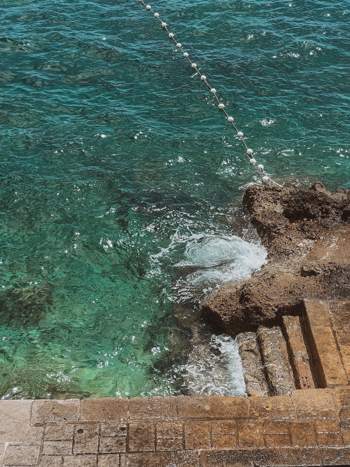 Close-up of ocean waves crashing against a stone wall with a rope barrier.