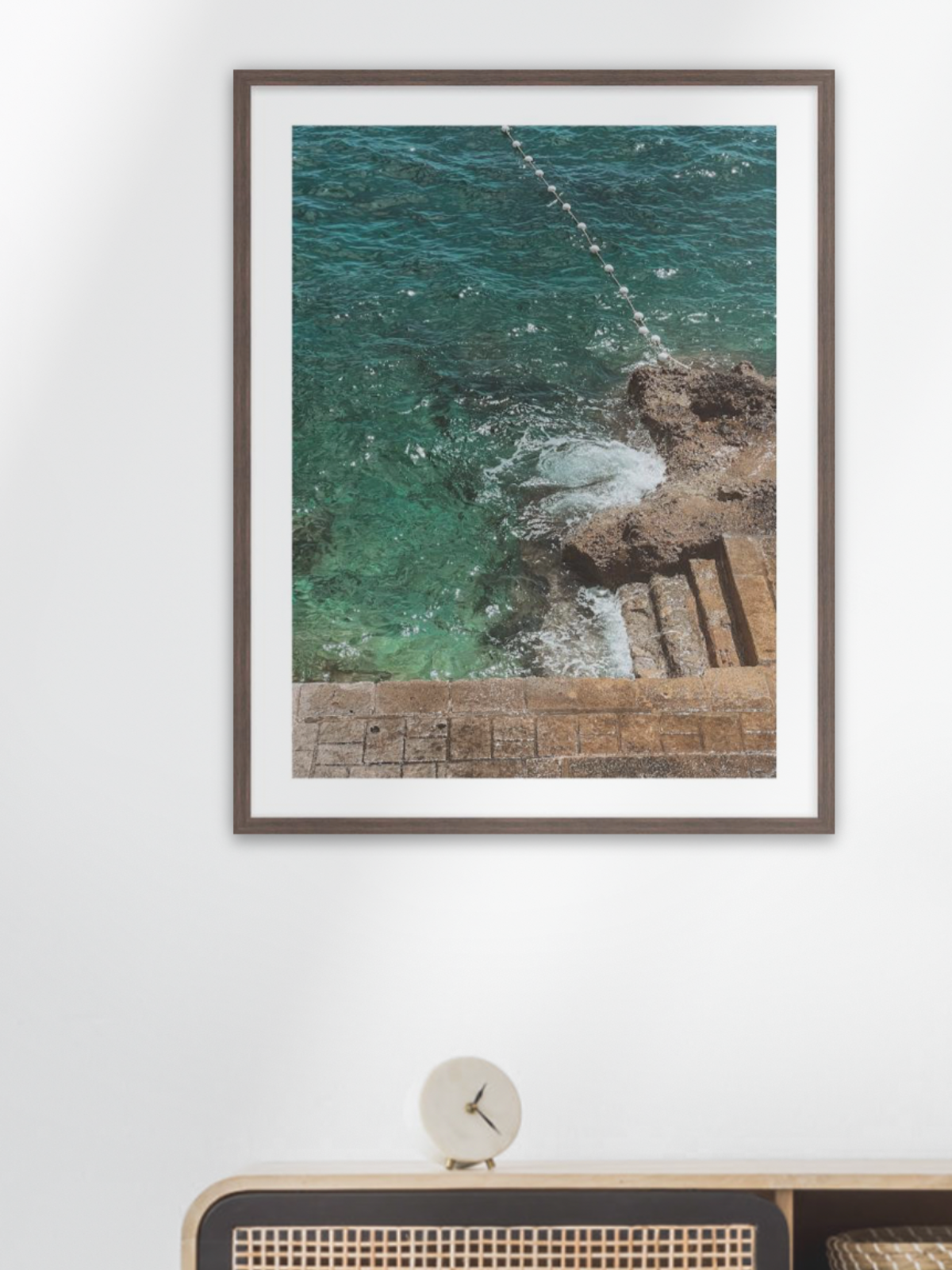 Framed photograph of a coastal scene on a white wall above a wooden console table.