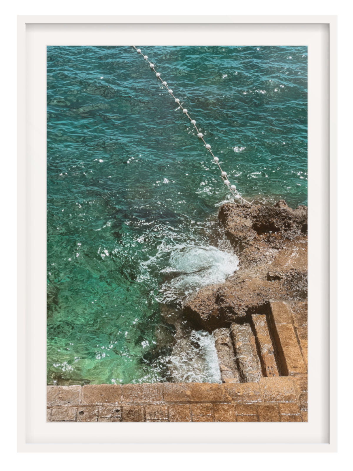 Framed photograph of a coastal scene with turquoise water and rocky shoreline.