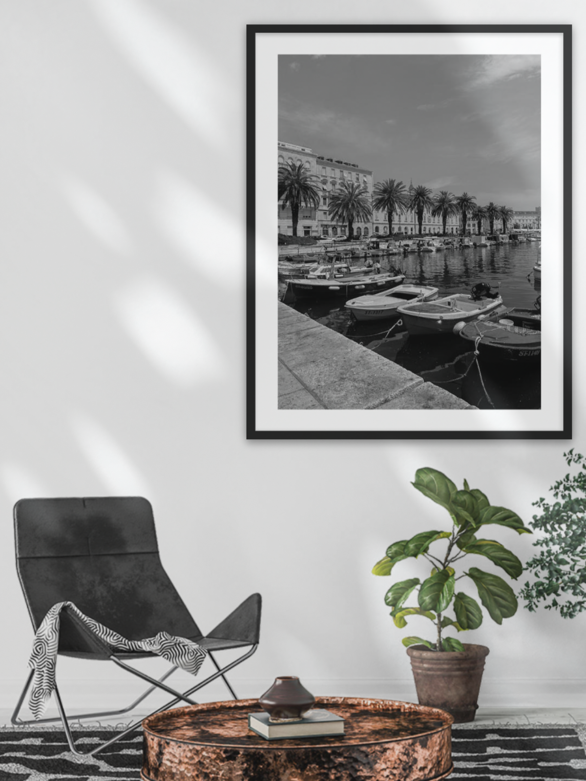 Framed black and white photograph of a waterfront scene on a wall above a chair and table.