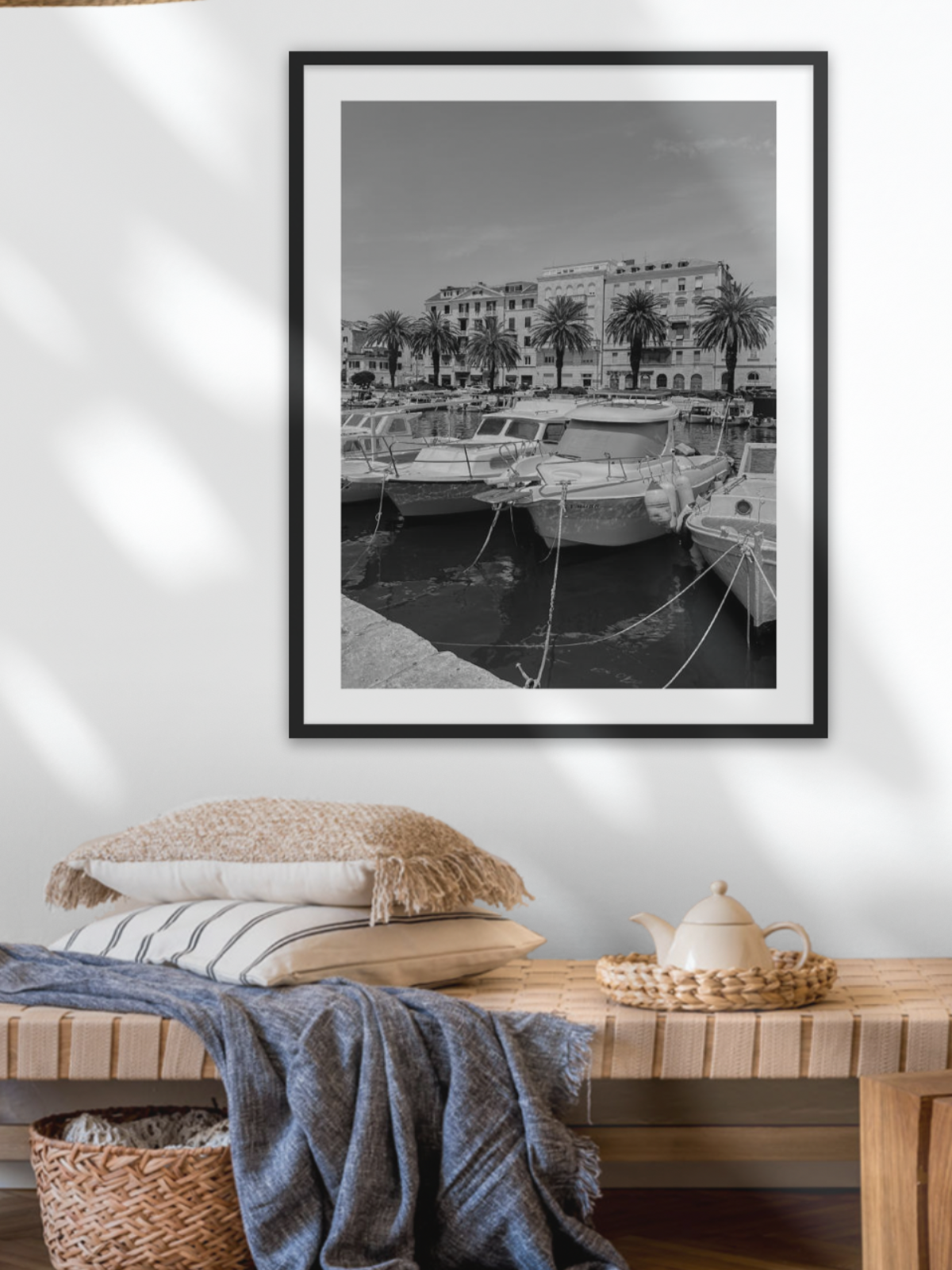 Framed black and white print of a harbor scene on a wall above a wooden console table.