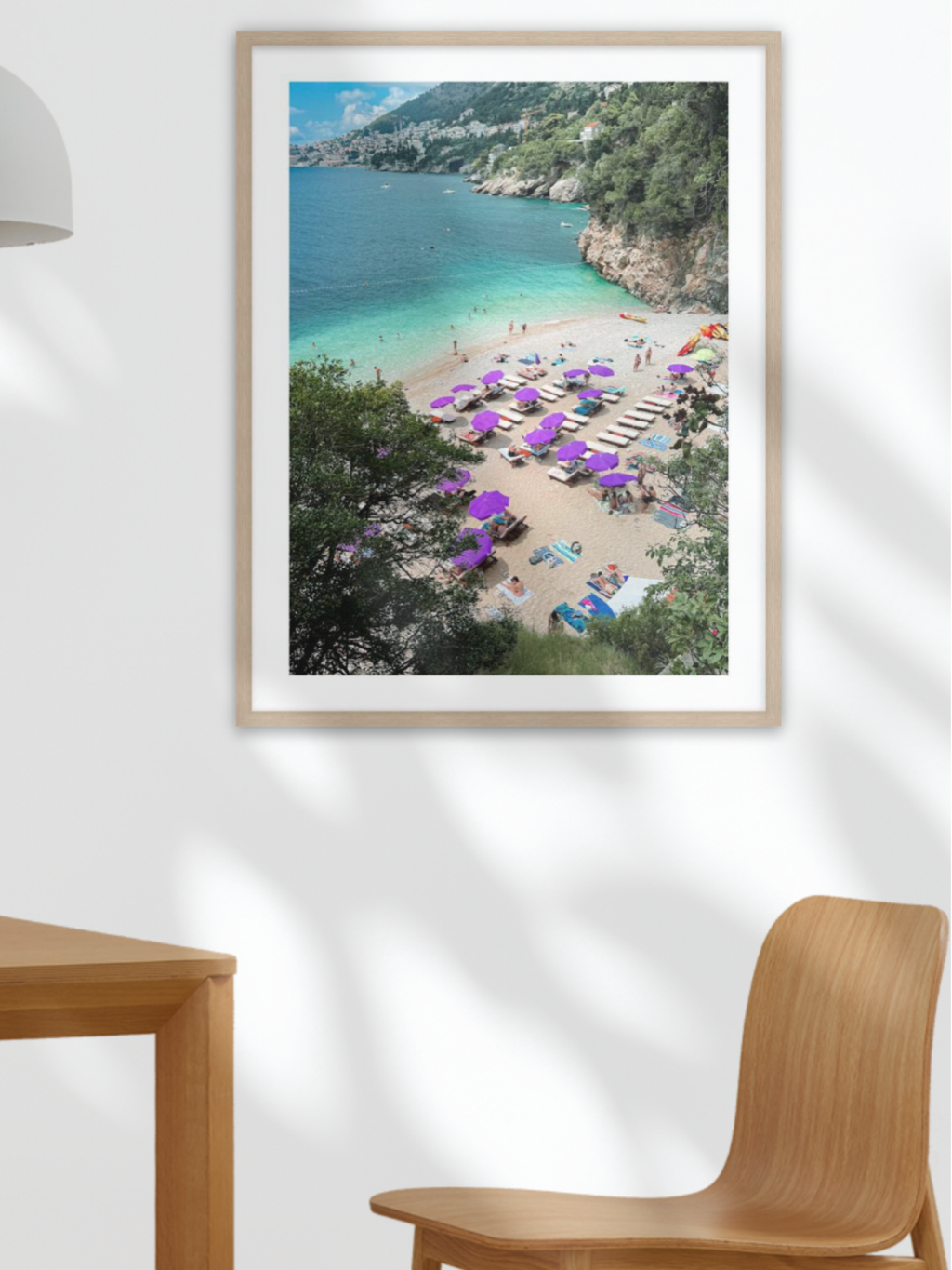 Framed photograph of a beach scene on a wall above a table with fruit and a plant.