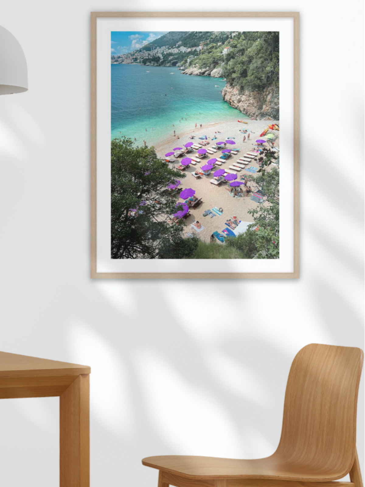 Framed photograph of a beach scene on a wall above a table with fruit and a plant.